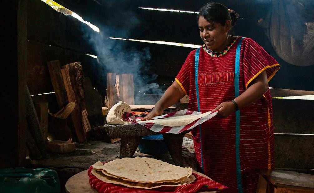 Las mujeres muelen maíz blanco para las tortillas y a un lado del fogón ponen la olla con chiles para la salsa.