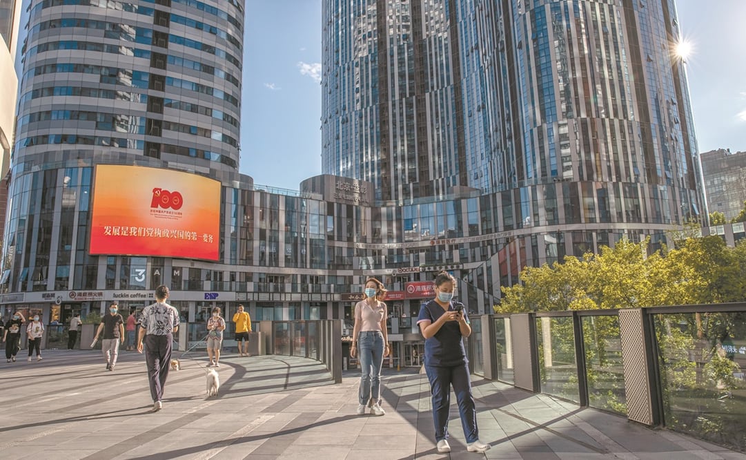 Personas con cubrebocas, junto a una pantalla que conmemora el centenario de la fundación del Partido Comunista de China en la zona comercial de Sanlitun, Beijing. Foto: Roman Pilipey. EFE