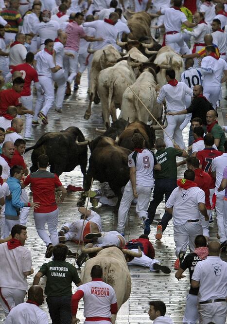  Varios mozos caen ante los toros de la ganadería gaditana de Fuente Ymbro a su paso por la calle de La Estafeta durante el primer encierro de los Sanfermines (EFE/Villar López)