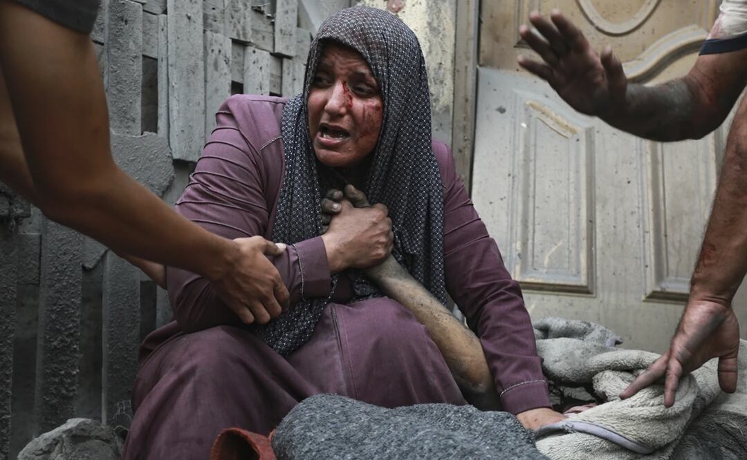 Una mujer palestina herida llora mientras sostiene la mano de su familiar muerto ante sui casa tras ataques israelíes que golpearon su vecindario en la Ciudad de Gaza. Foto: AP