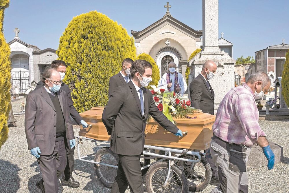 Empleados de una funeraria transportan el ataúd para una víctima de coronavirus, en un cementerio cerca de Cuneo, Italia. Foto: MARCO BERTORELLO. AFP
