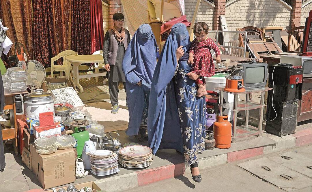 Mujeres con burka llevan en brazos a un niño por un mercado temporal de segunda mano en el barrio Chaman-e-Hozori de Kabul. FOTO: HOSHANG HASHIMI/ AFP.