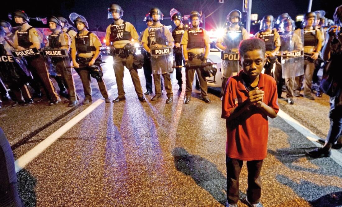 Un niño afroestadounidense permanece frente a un grupo de policías, durante las protestas por el aniversario de la muerte de Michael Brown en Ferguson (RICK WILKING. REUTERS)