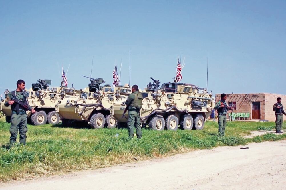 Esta imagen, tomada de video, muestra a combatientes kurdos de las Unidades de Protección Popular haciendo guardia mientras tropas de Estados Unidos toman posiciones en Siria. (AP)