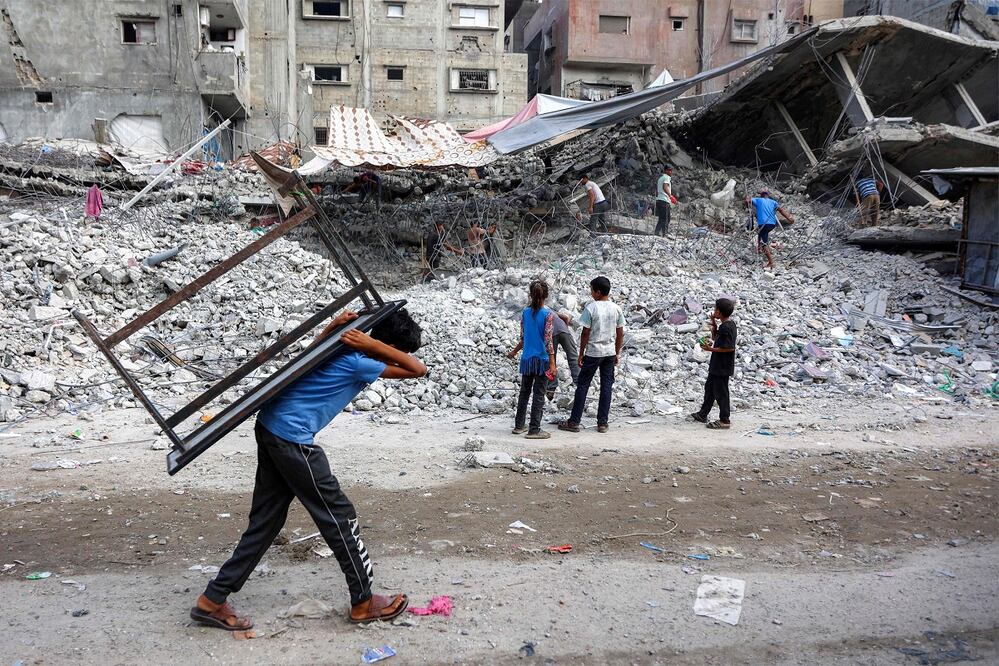 Un niño camina, cargado con una mesita, junto a los escombros de un edificio destruido durante la guerra con Israel, en Gaza. FOTO: OMAR AL-QATTAA. AFP