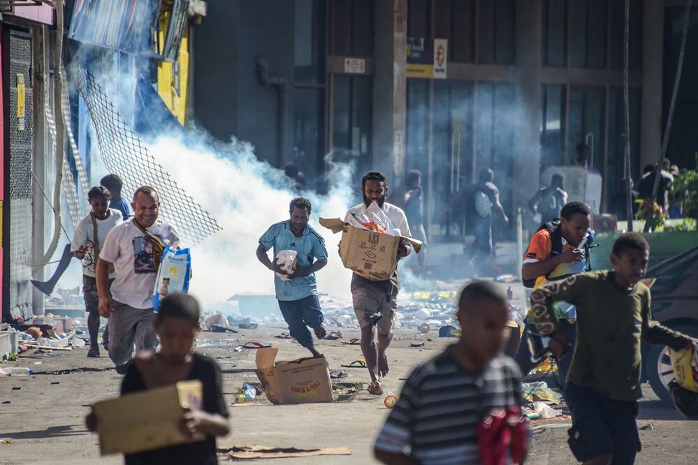La gente corre con mercancías mientras las multitudes abandonan las tiendas con productos saqueados en medio de un estado de malestar en Port Moresby el 10 de enero de 2024. Foto: AP