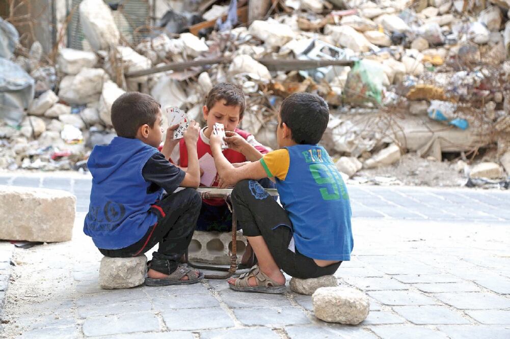 Niños sirios juegan cartas enfrente de un edificio destruido por los bombardeos, en Aleppo (ESPECIAL)