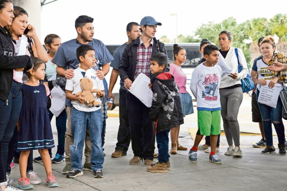 Familias de migrantes que ayer fueron liberadas de un centro de detención en McAllen, Texas, esperan un autobús. Foto/LOREN ELLIOTT. REUTERS