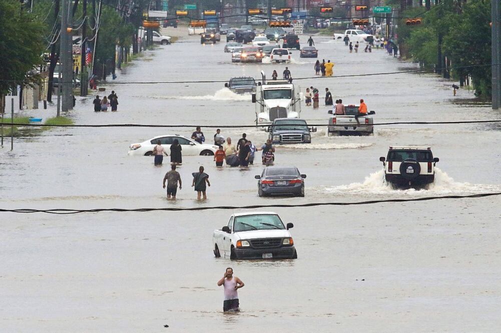 Personas caminan en el agua estancada en Telephone Road, entre decenas de vehículos inmóviles, a consecuencia del la tormenta tropical Harvey en Houston (THOMAS B. SHEA. AFP)