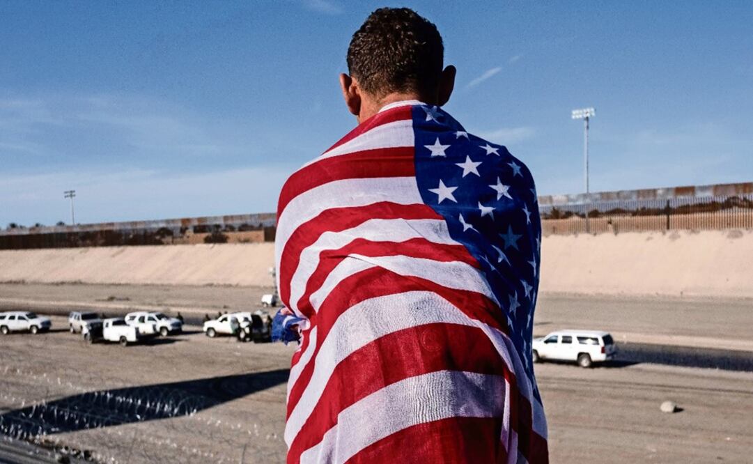 A Central American migrant wrapped in a U.S. flag looks at the almost dry riverbed of the Tijuana River - Photo: Guillermo Arias/AFP