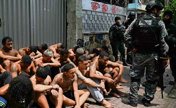 Agentes custodian a presuntos delincuentes arrestados durante el operativo en la favela Vila Cruzeiro. Foto: Mauro Pimentel / AFP