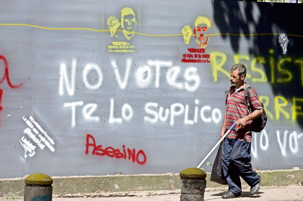 Un hombre camina frente a un muro en el que está escrito un mensaje en el que se hace un llamado a no votar en las elecciones de hoy en Caracas, Venezuela. (ARIANA CUBILLOS. AP)