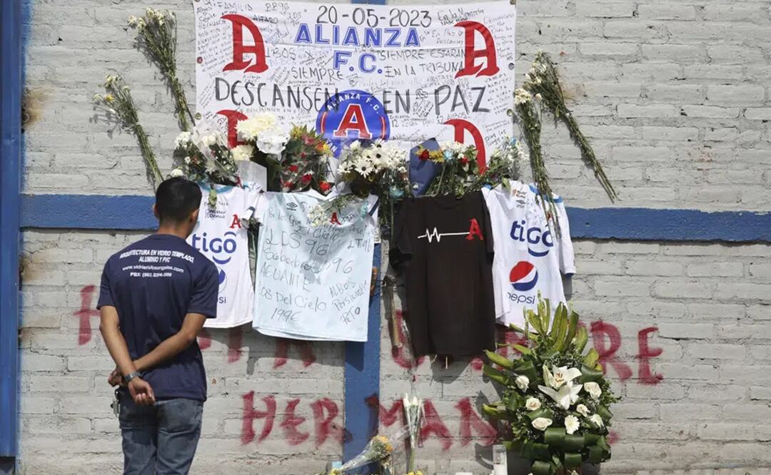 Un aficionado del Alianza se ve parado ante las ofrendas colocadas en memoria de aficionados muertos en una estampida en el estadio Cuscatlán ante el estadio, en El Salvador. Foto: AP