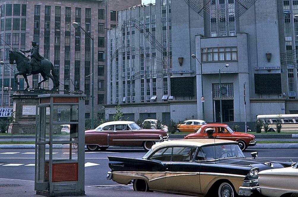 Una caseta telefónica de la década de los sesenta en el cruce del Paseo de la Reforma, Bucareli y la avenida Juárez, con el Caballito de Tolsá y el edificio de la Lotería Nacional de fondo. Imagen Col. Janice Watlzer
