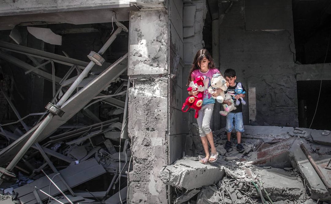 Niños palestinos rescatan sus juguetes de un edificio destruido durante un bombardeo israelí en Gaza. Foto: Anas Baba. AFP