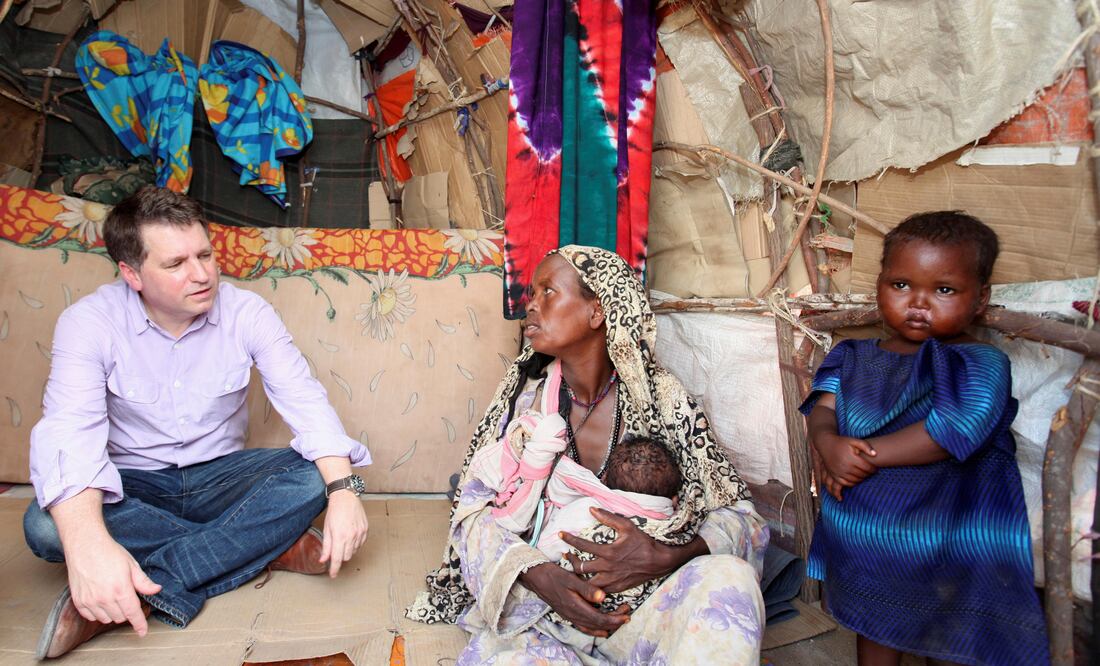 Imagen de 2012 que muestra a Justin Forsyth, entonces director de la organización británica Save The Children, habla con una desplazada somalí que carga a un bebé en brazos (Foto: Reuters)