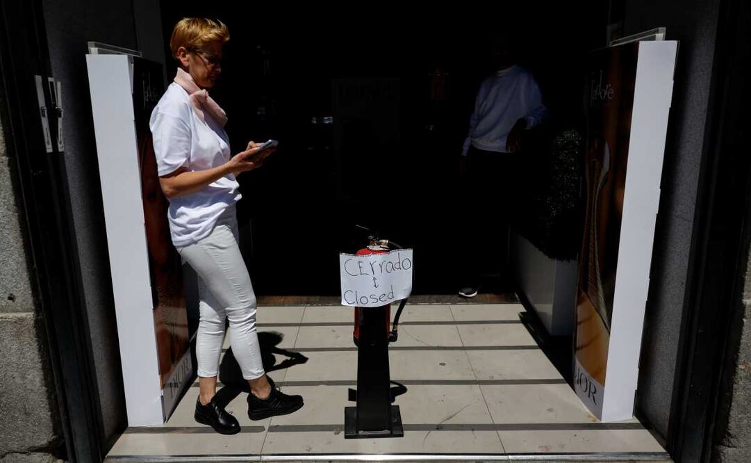 Una mujer revisa su móvil ante una tienda cerrada debido al apagón en un comercio del centro de Madrid, tras el corte de suministro eléctrico que afecta este lunes a España. Foto: EFE / Mariscal