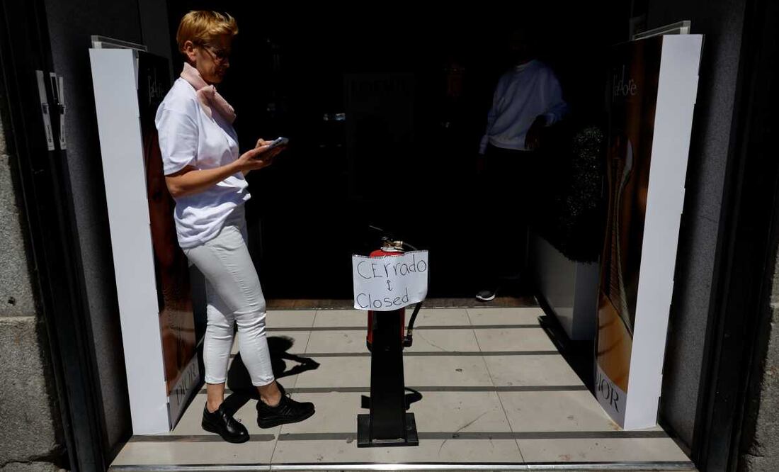 Una mujer revisa su móvil ante una tienda cerrada debido al apagón en un comercio del centro de Madrid, tras el corte de suministro eléctrico que afecta este lunes a España. Foto: EFE / Mariscal