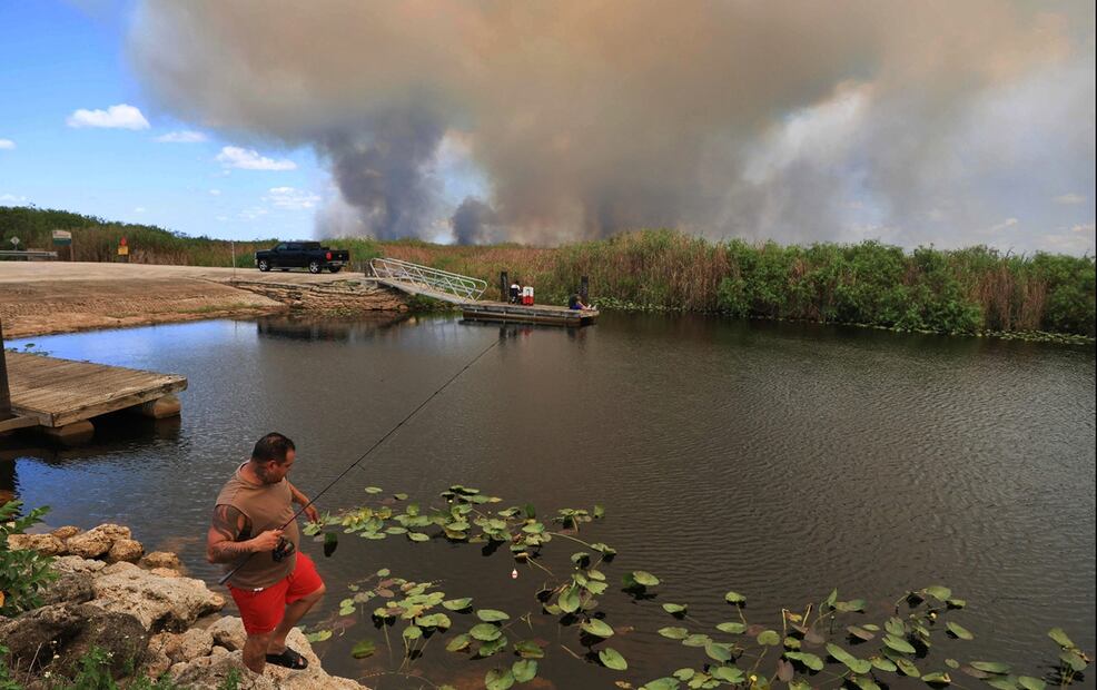 Varias personas pescan en un canal mientras el humo de un incendio forestal se eleva en los Everglades, Florida, el 20 de agosto de 2025. Estados Unidos ha registrado 44.130 incendios forestales en lo que va del año, un 68 % más que los 26.240 del mismo periodo del año anterior, según el National Interagency Fire Center del Gobierno de Estados Unidos.  Foto: AFP