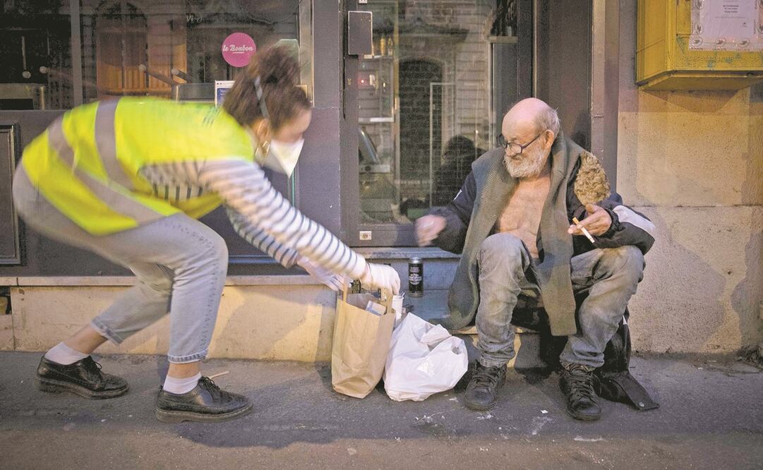 Una voluntaria da comida a una persona en situación de calle, en París, Francia, donde ayer se informó que se extenderá el confinamiento más allá del 15 de abril. Foto: JOEL SAGET. AFP