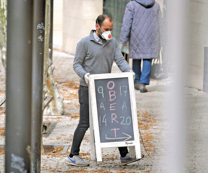 Comerciante. Un hombre con un cubrebocas sostiene un letrero de “abierto” en Barcelona. LLUIS GENE. AFP