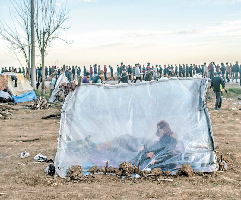 Una mujer siria aguarda con su hijo, mientras otros migrantes hacen fila para obtener comida en un campo en Pazarkule, en la frontera entre Grecia y Turquía, en marzo pasado. Foto: BULENT KILIC. AFP