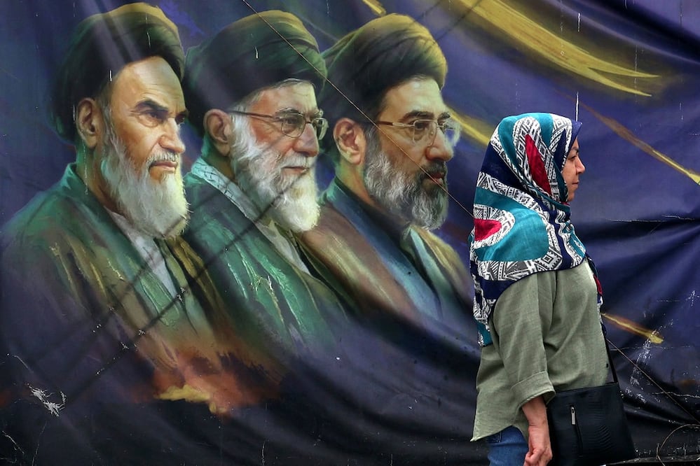 Una iraní pas junto a una pared con imágenes del fallecido ayatola Ali Jamenei, en Teherán. FOTO: AFP