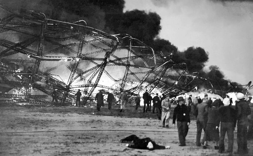 Restos de la estructura del Hindenburg tras el incendio que consumió su recubrimiento. Todavía se perciben llamas mientras algunos testigos se mantienen cerca del dirigible; un oficial del zepelín yace en el suelo después del siniestro. Foto: Wide World Photos/Wikimedia Commons.