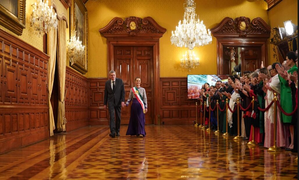 La presidenta Sheinbaum Pardo, portando la banda presidencial, y con vestido morado, recorrió los pasillos de Palacio Nacional para ser abanderada por la escolta del Heroico Colegio Militar de la Secretaría de la Defensa Nacional (Sedena). Foto: Presidencia