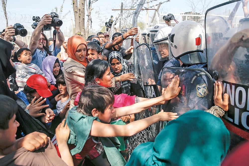 Policías intentaban ayer frenar a migrantes y refugiados que buscaban abrir una cerca en la frontera entre Grecia y Macedonia, en un campamento cerca de la localidad de Idomeni (MARKO DJURICA. REUTERS)