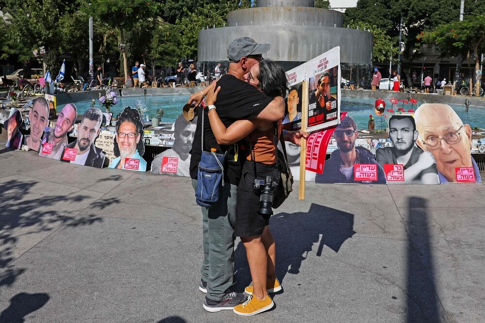 Israelíes se abrazan cerca de una fuente en Tel Aviv convertida en memorial por los rehenes que aún están en poder de Hamas. FOTO: AHMAD GHARABLI. AFP