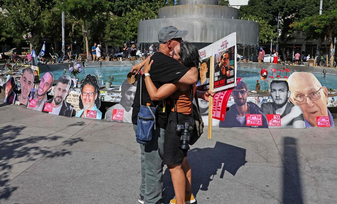 Israelíes se abrazan cerca de una fuente en Tel Aviv convertida en memorial por los rehenes que aún están en poder de Hamas. FOTO: AHMAD GHARABLI. AFP