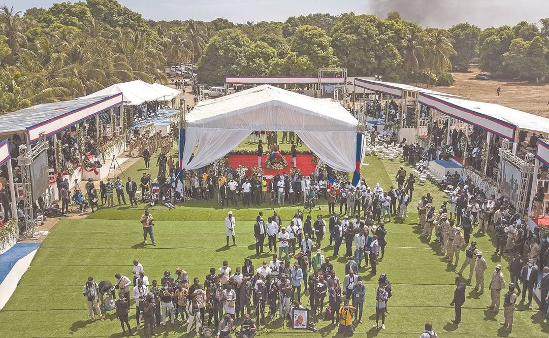 Asistentes al funeral del asesinado presidente haitiano Jovenel Moïse; el humo de fondo se eleva desde donde los partidarios queman neumáticos para protestar por su asesinato y no poder entrar a la ceremonia, en Cabo Haitiano. Foto: Matias Delacroix/ AP.,