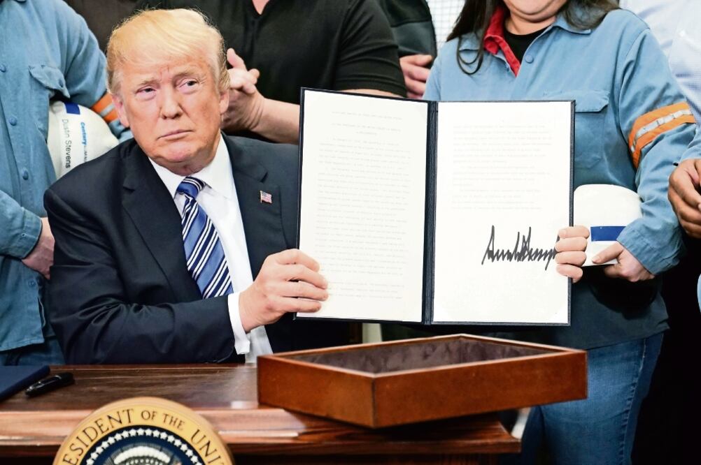 Donald Trump, presidente de EU, muestra una de las dos órdenes ejecutivas para imponer tasas aduaneras a las importaciones de acero y aluminio (MANDEL NGAN. AFP)