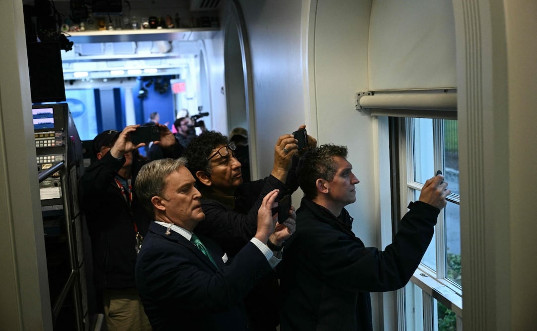Reporteros en la sala de prensa de la Casa Blanca intentan captar con sus teléfonos lo que ocurre en el exterior tras el confinamiento en Washington (23/05/2026). Foto: AFP