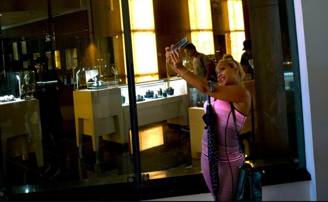 Teenagers and young adults pose in front of shop windows to take selfies and post them on Facebook 