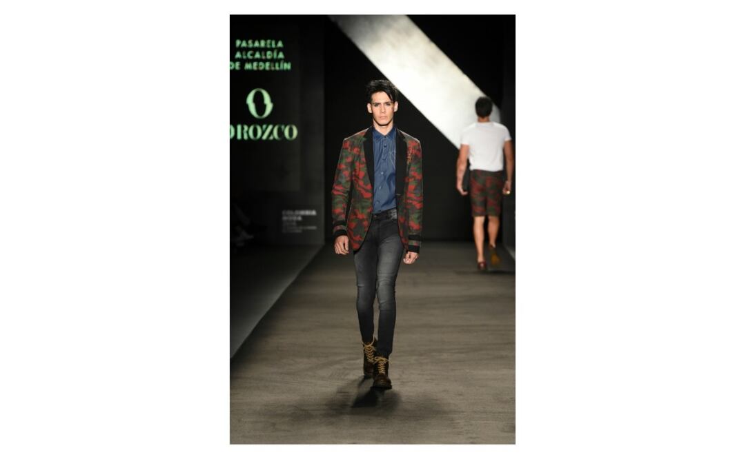 Saco con estampado militar en rojo, negro y verde, camisa azul de cuello, pantalón de mezclilla deslavado y botas Cherry con agujetas amarillas Doctor Martens.