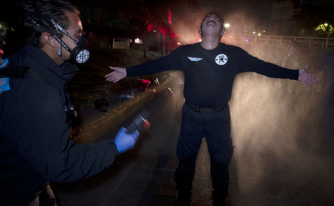 El paramédico Óscar Becerril descontamina a su compañero César Ávila después de una llamada nocturna para recoger a un paciente con Covid-19, en su base Troya en Iztapalapa Fotos: AP)