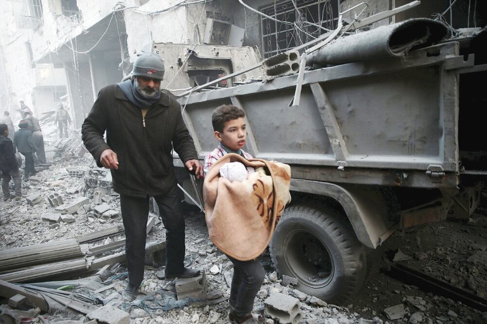 Un niño sirio carga a un bebé en la ciudad de Douma, en Damasco, lugar que los activistas dicen fue atacado por fuerzas rusas (BASSAM KHABIEH. REUTERS)