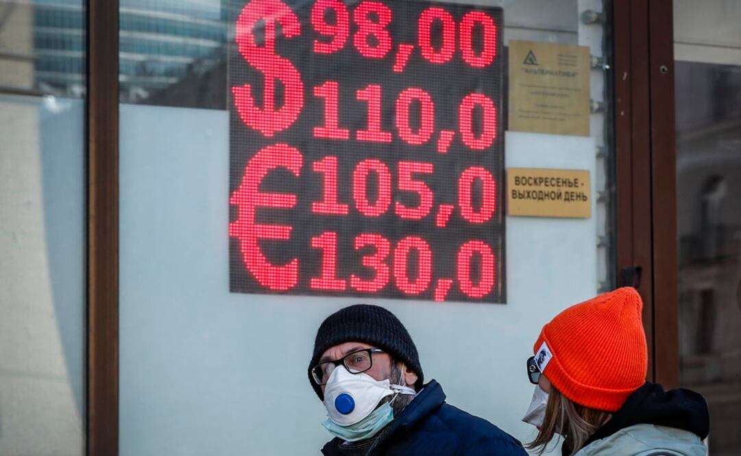 Los rusos caminan frente a una oficina de cambio con una pantalla que muestra las tasas de cambio del dólar estadounidense y el euro al rublo ruso en Moscú. Foto: EFE