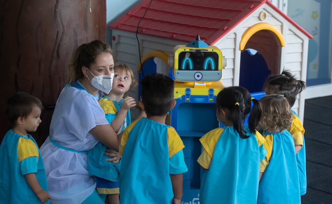 Una maestra les enseña a unos niños un robot que mide la temperatura. Foto: AP /Paul White, archivo
