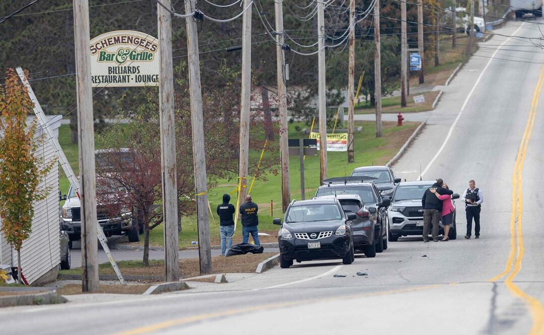Una mujer abraza a un agente de la ley mientras investigan fuera del lugar de un tiroteo masivo en Schemengees Bar and Grille en Lewiston, Maine. Foto: AFP