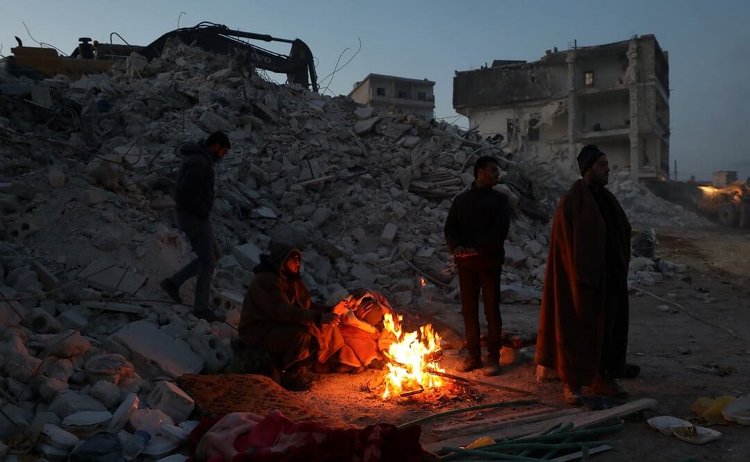 La gente se calienta alrededor de un fuego cerca de un edificio derrumbado después de un terremoto en Idlib, Siria. Foto: EFE