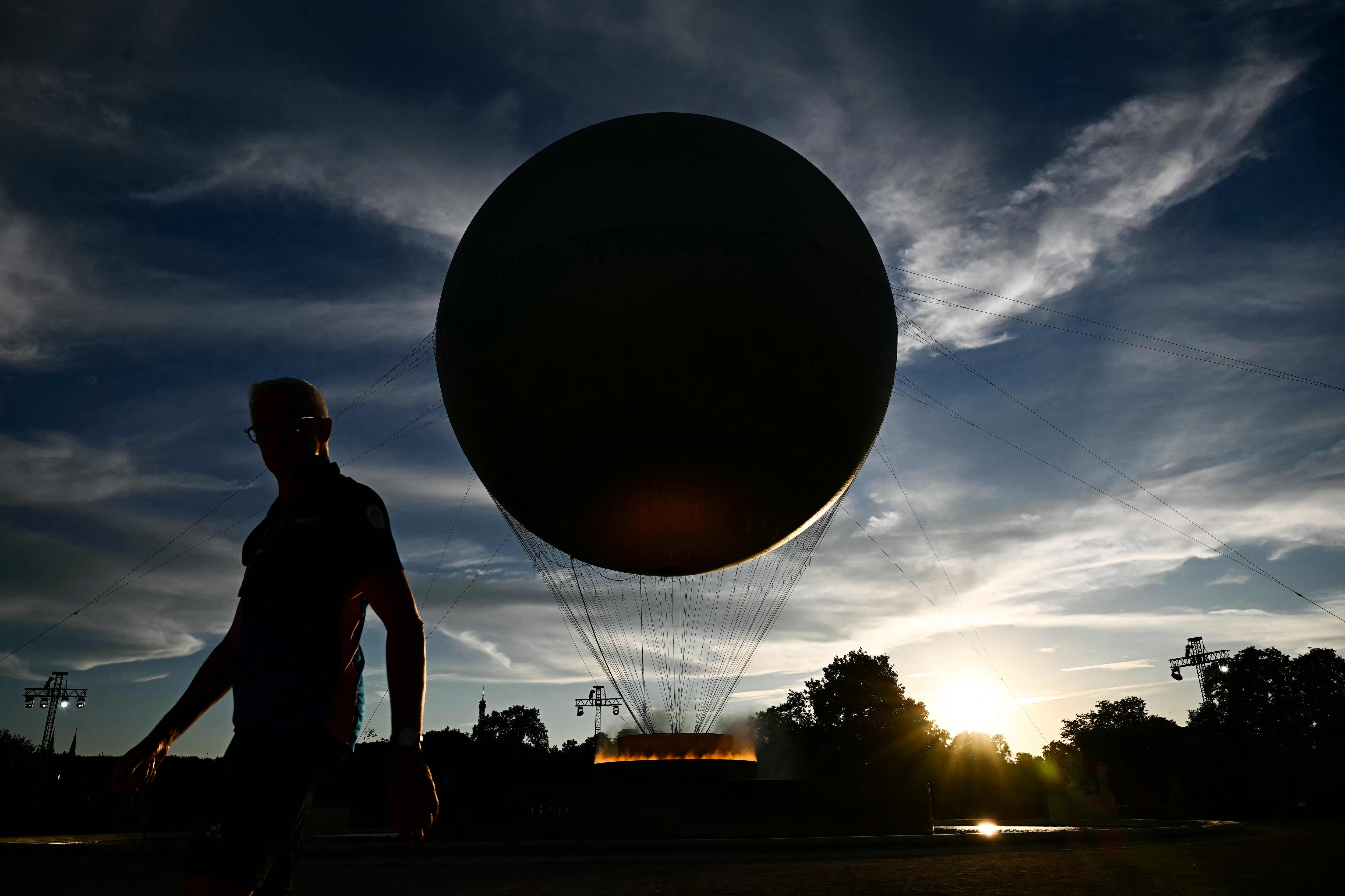 Un hombre caminando en las calles parisinas, con el atardecer cayendo en el pebetero olímpico - Foto: AFP