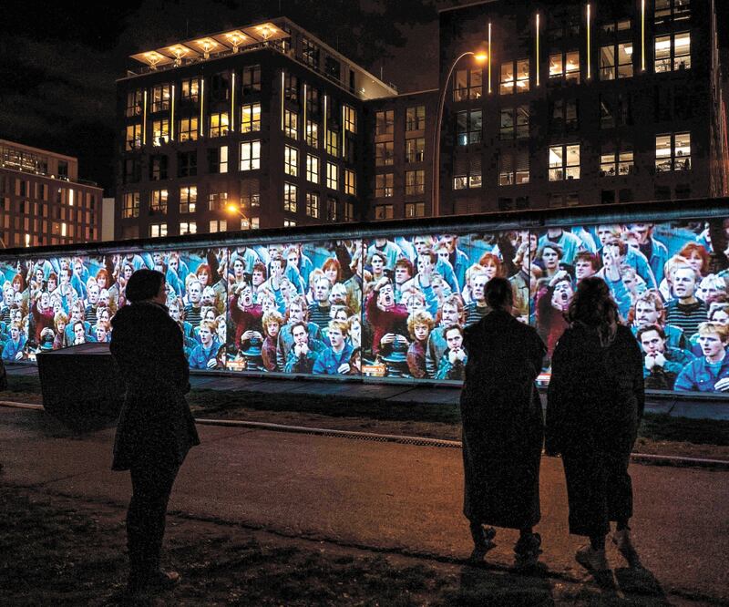 Alemanes observan una proyección de las manifestaciones en la Alemania del Este, en la East Side Gallery, en Berlín. Foto: JOHN MACDOUGALL. AFP