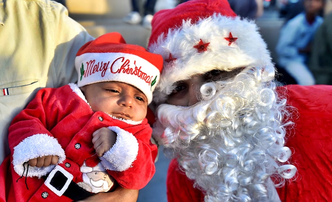 Un bebé y un adulto disfrazados de Santa Claus durante un desfile previo de Navidad en una carretera de Karachi, Pakistán. Foto: EFE