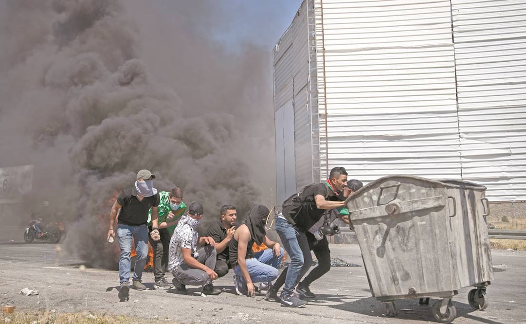 Los manifestantes palestinos se protegen durante los enfrentamientos contra las fuerzas israelíes en el puesto de control de Hawara, Nablus. En Cisjordania los violentos disturbios han dejado 11 palestinos muertos. Foto: Mahmoud Illean/ AP.