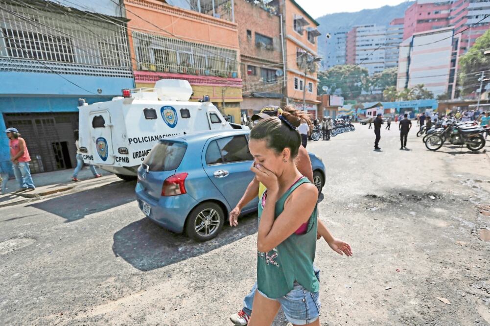 Una mujer cubre su boca del gas lacrimógeno disparado por la Policía Nacional Bolivariana afuera de una tienda de comestibles y licores para dispersar a saqueadores durante una protesta registrada ayer en Caracas (FERNANDO LLANO.AP)
