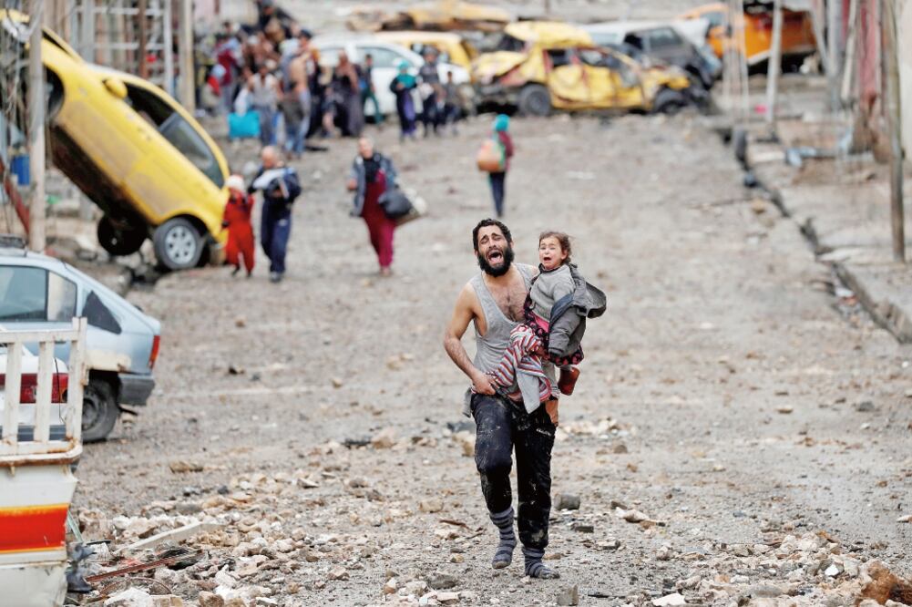 Un padre y su hija huyen de los combates en Mosul, en una imagen de marzo de este año difundida ayer por la agencia Reuters, que contó historias de los lugareños (GORAN TOMASEVIC. REUTERS)