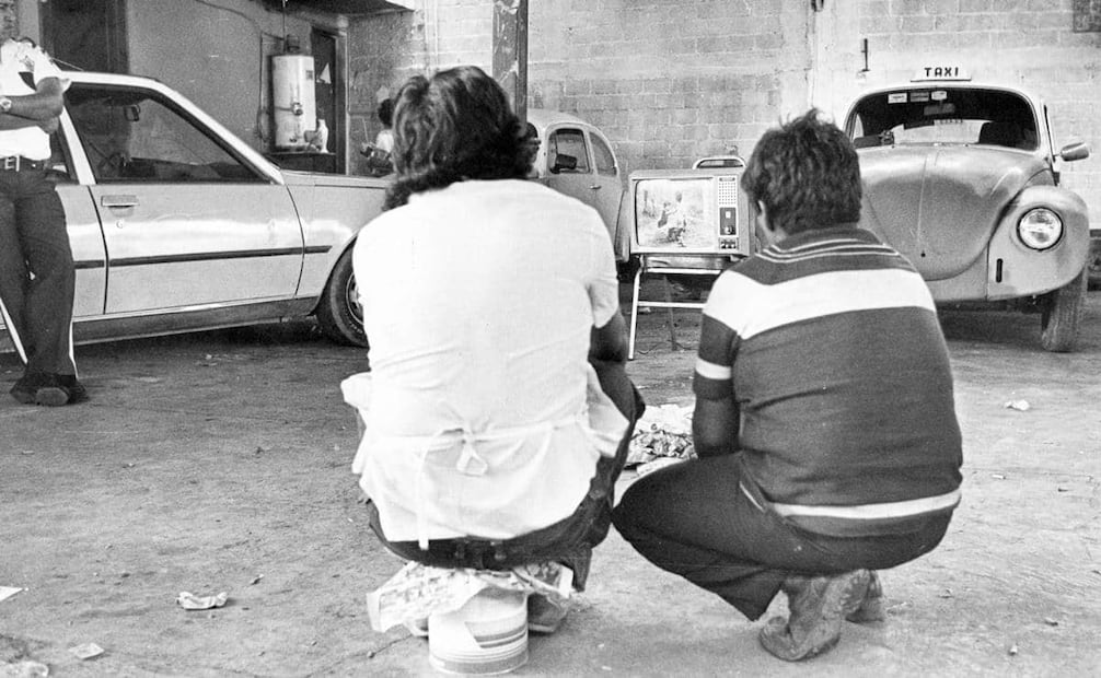 Capitalinos viendo la inauguración del mundial México 86 en una pequeña televisión blanco y negro, en un estacionamiento. La Secretaría de Comunicaciones y Transportes y Televisa se unieron para formar Teleméxico, un sistema de transmisión internacional exclusivo para el mundial de 1986. Foto: Archivo EL UNIVERSAL.